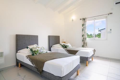 1 dormitorio con 2 camas y ventana en Villa des Pentas – Chaleureuse Villa moderne avec piscine, en Baie-Mahault