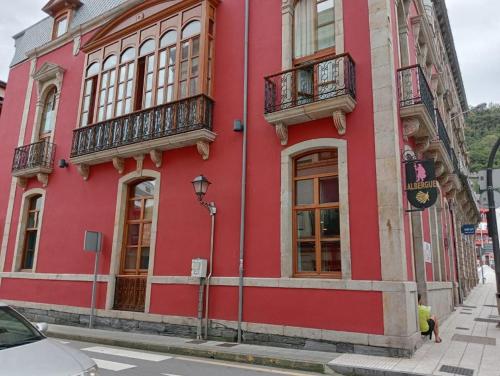 a red building with windows and balconies on a street at Albergue de Peregrinos Villa de Luarca in Luarca