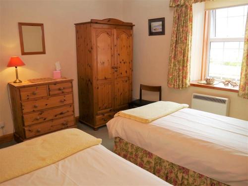 a bedroom with two beds and a dresser and a window at Branta Cottage in Dumfries