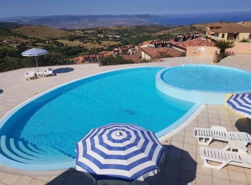 a blue swimming pool with an umbrella and some chairs at Casa Smeralda - Piscina e vista sul Mare! in Trinità dʼAgultu
