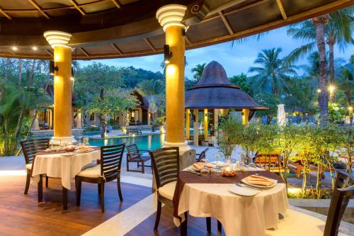 an outdoor dining area with tables and chairs and a pool at The Village Resort - SHA Plus in Karon Beach