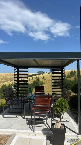 a picnic table and benches under a pavilion with a field at Wild nest Deer Lux in Zlatibor