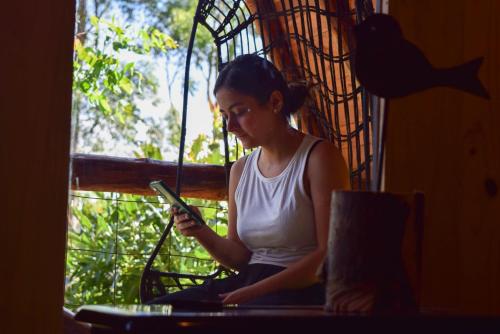 a woman sitting on a window looking at her cell phone at Glamping con jacuzzi cerca a Medellin in Guarne