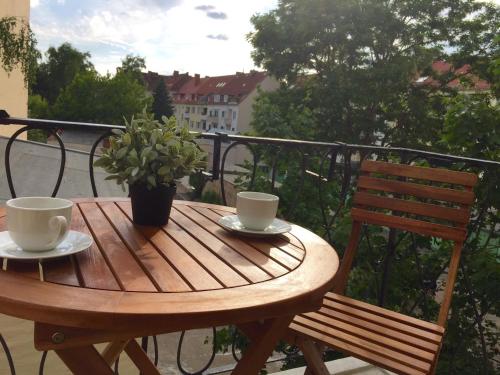 una mesa de madera con 2 tazas y una maceta en el balcón en Apartment H50 en Hannover