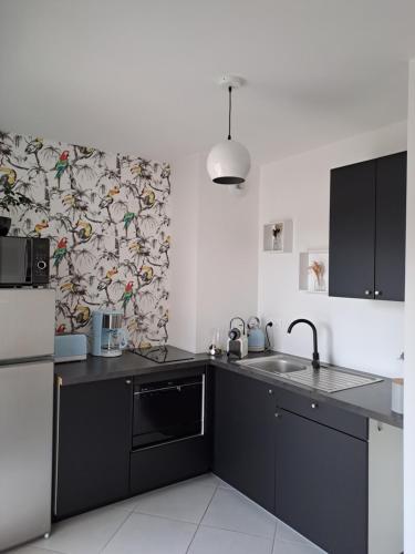 a kitchen with black cabinets and a patterned wall at Logement neuf dans résidence calme parking gratuit in La Rochelle