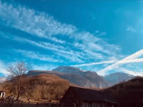 um céu azul com nuvens e uma casa e montanhas em Shpija e Gjyshit Vuthaj em Gusinje