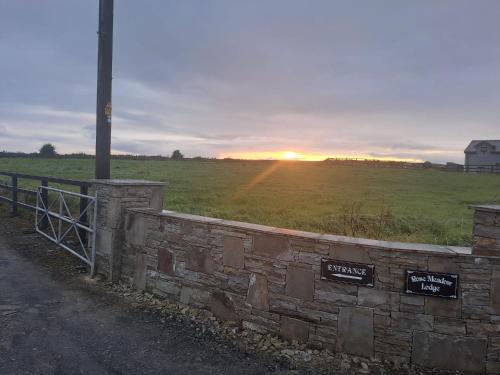 a sunset over a field with a stone wall at Rose Meadow Lodge in Liscannor