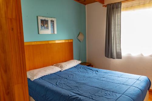 a bedroom with a bed with a blue blanket and a window at Departamentos Aquario Papudo in Papudo