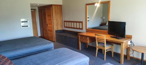 a hotel room with a desk and a bed and a mirror at Distinction Mackenzie Country Hotel in Twizel