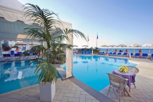 a large swimming pool with a table and a palm tree at Hotel Solemar Beach & Beauty SPA in Ischia