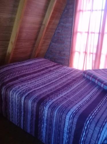 a bed with a striped blanket in a room with a window at Cabañas Las Acacias in Trevelín