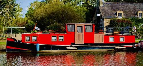 uma casa de barco vermelha sentada na água em Magnifique péniche remorqueur à louer em Évran