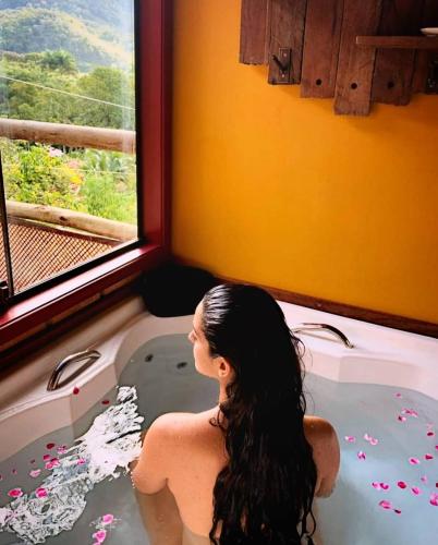 a woman sitting in a bath tub looking out a window at Chalé Canto da Colina-Lumiar in Lumiar