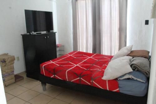 Schlafzimmer mit einem Bett mit einer roten Bettdecke und einem TV in der Unterkunft Amplia Casa/Residencia a 15 Minutos de playa Miramar y Altama in Tampico