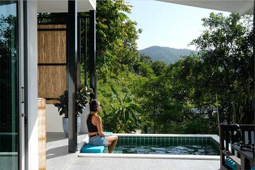 una donna seduta su una sedia accanto alla piscina di The Love Nest - Stylish One Bed House a Ban Chalok Lam