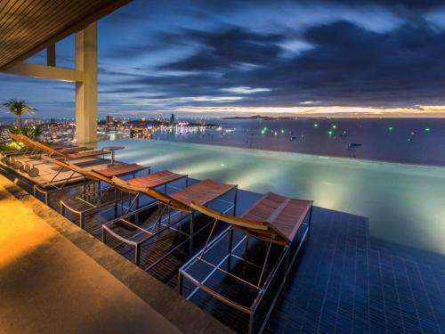 a hotel swimming pool with chairs in the water at night at 芭提雅Fnb Central 无边泳池 in Pattaya