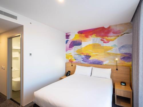 a bedroom with a white bed and a painting on the wall at Ibis Styles Hobart in Hobart