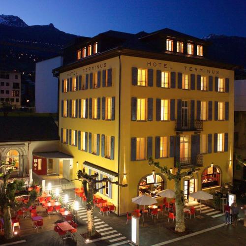 a hotel with tables and umbrellas in front of a building at Hôtel Au Terminus in Sierre