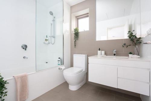 a white bathroom with a toilet and a shower at 'The Peak' Resort-style Balcony Abode in the Metro in Sydney