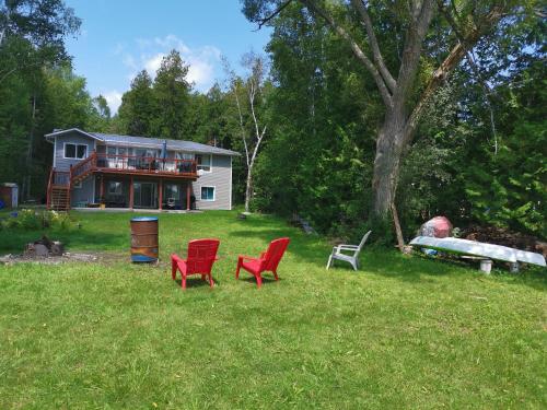 a house with red chairs in front of a yard at Pigeon Lake Cottage in Kawartha Lakes