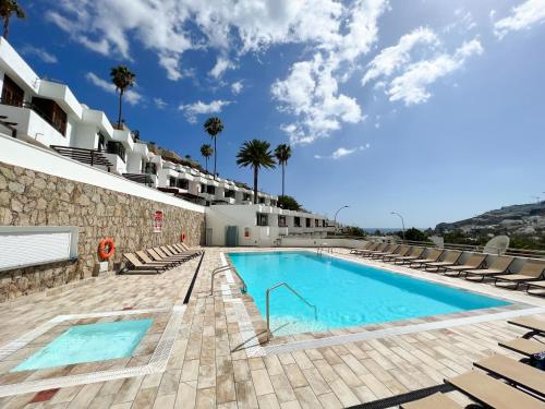 einen Pool mit Chaiselongues neben einem Gebäude in der Unterkunft Sonnige, neu renovierte Ferienwohnung Casa Las Fresas in Puerto Rico de Gran Canaria