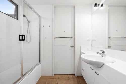 La salle de bains blanche est pourvue d'un lavabo et d'une douche. dans l'établissement Spindrift, à Point Lonsdale