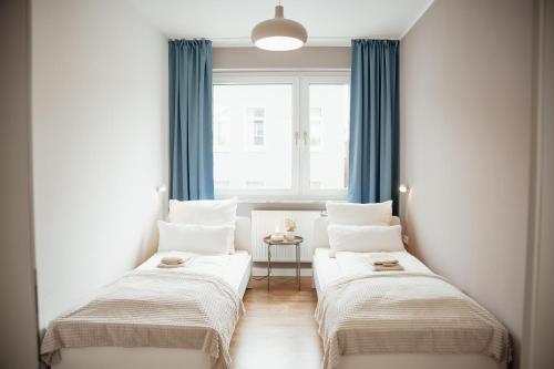 2 Betten in einem Zimmer mit blauen Vorhängen und einem Fenster in der Unterkunft Gemütlich, hell & zentral in Wilhelmshaven