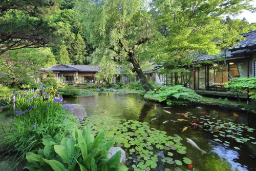 a pond in a garden with flowers and a house at Tachibanaya in Tsuruoka