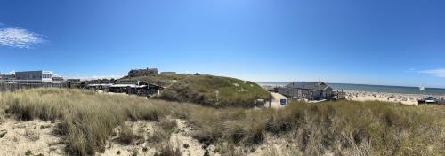 un groupe de personnes sur une plage avec une colline dans l'établissement Neptunus Appartementen, à Bergen aan Zee