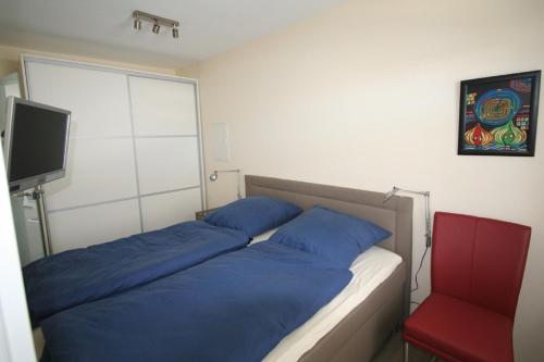 1 dormitorio con cama con almohadas azules y silla roja en Miramar App 708 inkl WLAN, en Grömitz