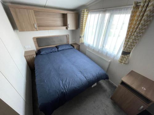 a small bedroom with a blue bed and a window at 8 Berth Static Caravan - Holiday Resort Unity Brean in Berrow