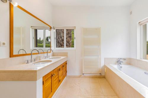 La salle de bains est pourvue d'une baignoire, de deux lavabos et d'une baignoire tubermottermott. dans l'établissement Villa Jardim do Paraiso, à Mexilhoeira Grande