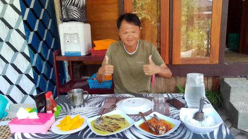 a man giving a thumbs up next to a table with food at Naca Homestay in Manado