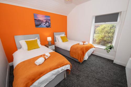 twee bedden in een kamer met oranje muren en een raam bij Versatile Cozy & Spacious Comfort Hull Apartments in Hull