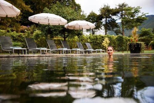 a woman standing in a swimming pool with chairs and umbrellas at Octant Furnas in Furnas