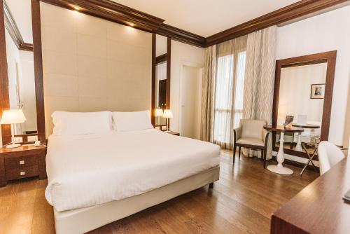a bedroom with a large white bed and a desk at Palazzo Bezzi Hotel in Ravenna