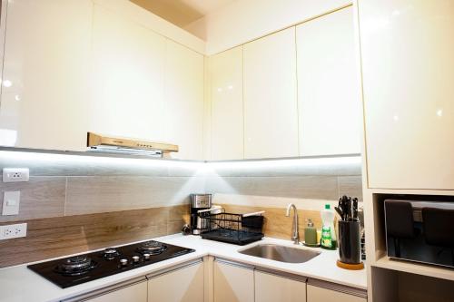 a kitchen with white cabinets and a stove and a sink at Modern Designed Studio Condo Near Ayala Centrio in Cagayan de Oro