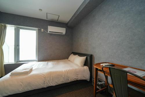 a bedroom with a bed and a desk and a window at Residence Hotel Stripe Sapporo in Sapporo
