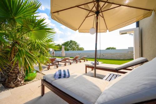 a patio with lounge chairs and an umbrella at Villa Linnelle seaview- Rovinj, heated pool in Burići