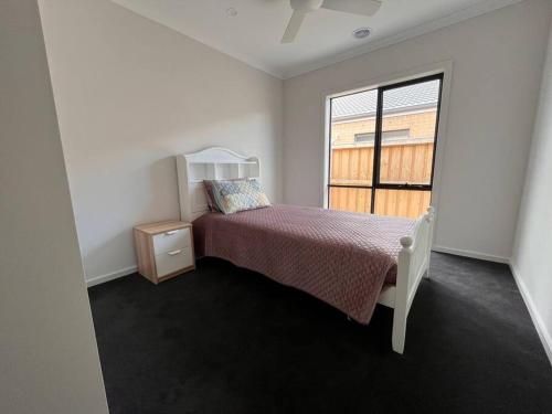 een witte slaapkamer met een bed en een raam bij Spacious 4 bedroom home in Weir Views near Warrawong Estate in Melton