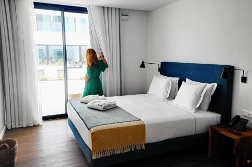 Pêro Teive Bay Apartments Hotel في بونتا ديلغادا: امرأة تقف في غرفة الفندق مع سرير