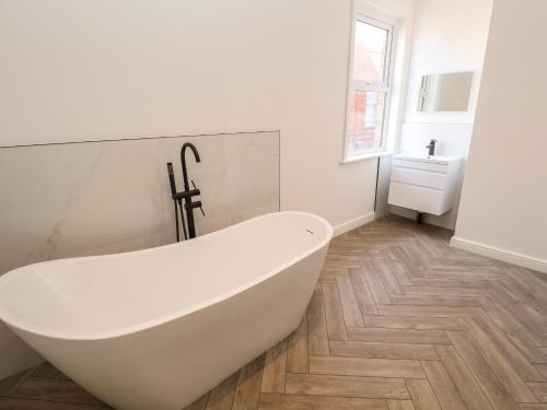 a white bath tub in a bathroom with a wooden floor at Carlton House in Skegness