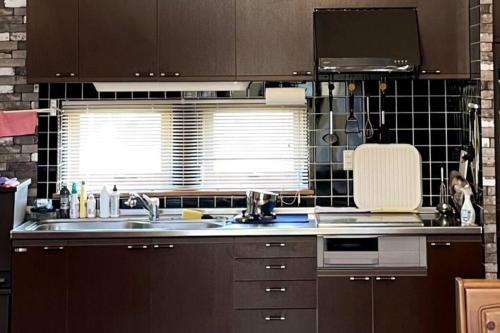 a kitchen with brown cabinets and a sink and a window at コテージR 広々空間と自然豊かなエリアでRelaxステイ バーベキューセットあり4名様まで同一料金 in Shiraoi