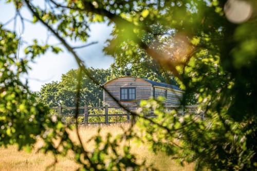 a large wooden barn in a field with trees at Monkwood Shepherds Hut - Ockeridge Rural Retreats in Worcester