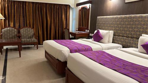 a hotel room with two beds and a chair at Hotel Annamalai International in Puducherry