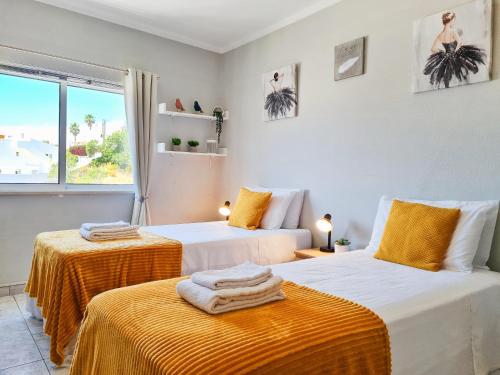 1 dormitorio con 2 camas con sábanas de color naranja y ventana en CASA TÔMBUA - Pool - Beach & Center 300m - AC - WiFi, en Carvoeiro