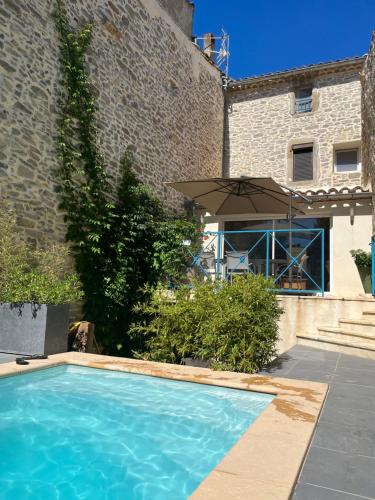 - une piscine en face d'un bâtiment avec un parasol dans l'établissement Chez Elia, pour les amoureux des vieilles pierres, à Cesseras