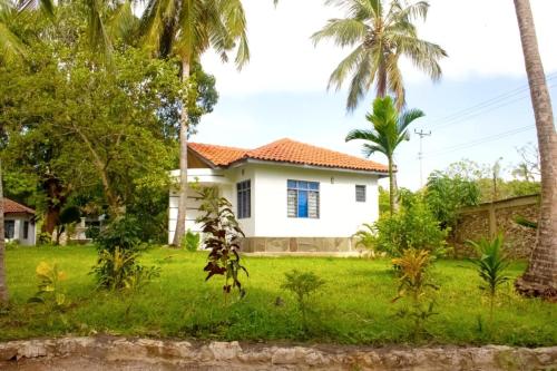 a white house with palm trees in a yard at Cycad Palm Diani in Diani Beach