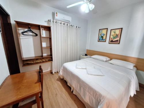 a bedroom with a white bed and a wooden table at Hotel Itapema in Valinhos