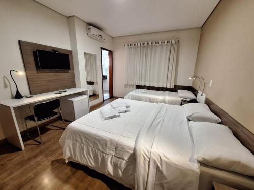 a bedroom with two beds and a desk and a television at Hotel Itapema in Valinhos